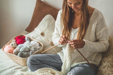 Beautiful girl knits a warm sweater on the bed. Knitting as a hobby. Accessories for knitting.の写真素材