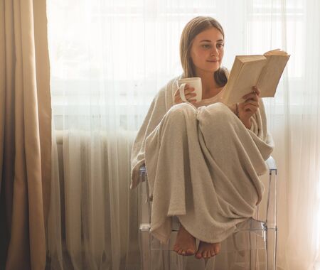 Beautiful girl is reading a book with a cup of hot tea. Autumn Winter Time. Cozy home.の写真素材