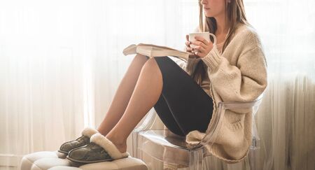 Beautiful girl is reading a book with a cup of hot tea. Autumn Winter Time. Cozy home.の写真素材