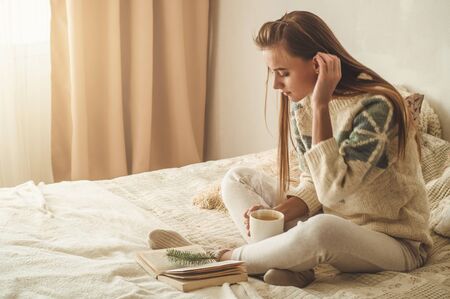 Beautiful girl is reading a book with a cup of hot tea. Autumn Winter Time. Cozy home.の写真素材