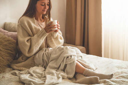Cozy Autumn winter evening. Woman drinking hot tea and relaxing at home. Comfy lifestyleの写真素材