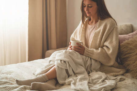 Cozy Autumn winter evening. Woman drinking hot tea and relaxing at home. Comfy lifestyleの写真素材
