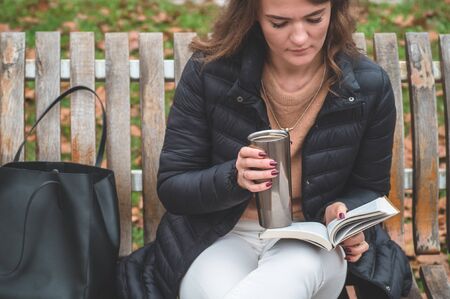 Girl holds book in her hands. The girl sitting on a bench, reading a book. Rest and readingの写真素材