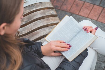 Girl holds book in her hands. The girl sitting on a bench, reading a book. Rest and readingの写真素材