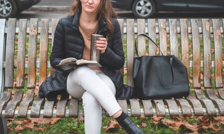 Girl holds book in her hands. The girl sitting on a bench, reading a book. Rest and readingの写真素材