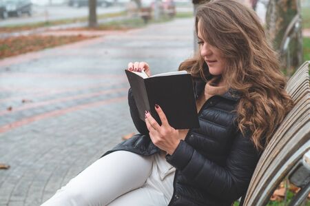 Girl holds book in her hands. The girl sitting on a bench, reading a book. Rest and readingの写真素材