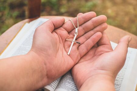 Woman holding a the cross in hand against the background of the bible. Hands folded in prayer...