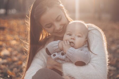 Happy family on autumn walk. Mother holds little son in her arms and enjoying the beautiful autumn...