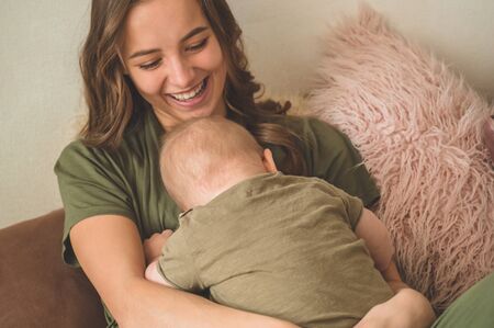 Home portrait of a baby boy with mother on the bed. Mom holding and kissing her child. Mother day conceptの写真素材