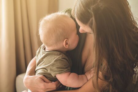 Home portrait of a baby boy with mother on the bed. Mom holding and kissing her child. Mother day...
