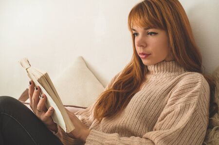 Attractive young woman is reading a book at home. Thoughtful girl reading important book. Reading...