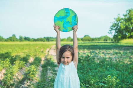 Protection and love of earth. Little girl holding planet in hands against green spring background. Earth day holiday concept. Environmental Conservationの写真素材
