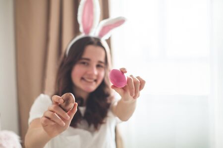 Teenager girl with Easter ears and a wicker Easter basket on a bed in a living room. Emotions. Easter conceptの写真素材