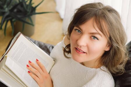 Beauty young woman is reading a book at home. Thoughtful girl reading important book. Reading and...