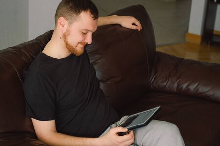 Technology, home. Male working with the tablet computer and sitting on chair at home.