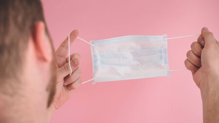 A Man holds viral mask on a pink background, wearing face protection in prevention for coronavirus. COVID-19 Pandemic Coronavirusの写真素材
