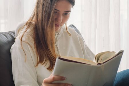 Reading and development. Beauty young woman is reading a book at home. Thoughtful girl reading important book.の写真素材