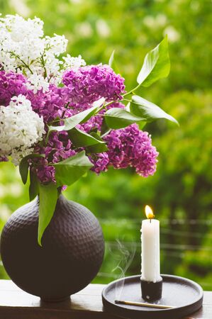 Blooming spring lilac flowers and burning candle in a candlestick. Spring background.の写真素材