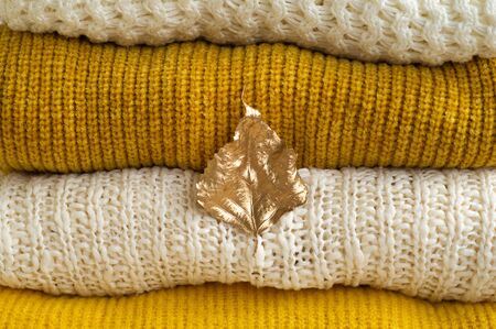 Autumn winter concept. Pile of knitted clothes with autumn gold leaves, warm background, knitwear.の写真素材