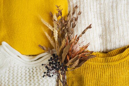 Pile of knitted clothes yellow white color with dried flower bouquet. Autumn winter concept. Copy Space.の写真素材