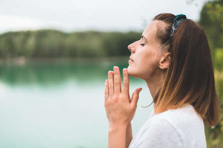 Woman closed her eyes, praying in outdoors. Hands folded in prayer concept for faith, spirituality and religion. Peace, hope, dreams conceptの写真素材
