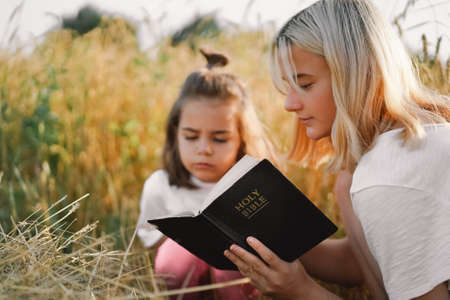Girls reading holy bible in a wheat field. Study the holy bible together.の写真素材