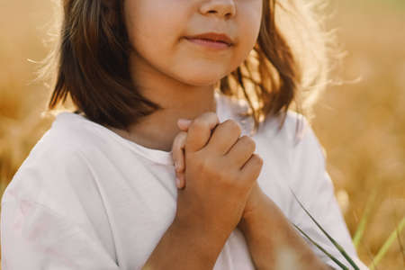 Little Girl closed her eyes, praying in a field wheat. Hands folded in prayer. Religion conceptの写真素材