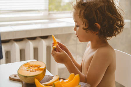 Cute beautiful little boy eating fresh melon. Healthy food, childhood and development. Happy kid at home.の写真素材