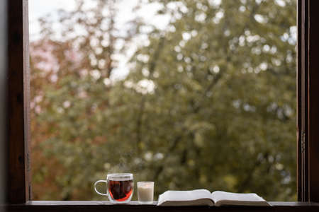A cup of hot tea and an open book on a vintage windowsill. Read and rest