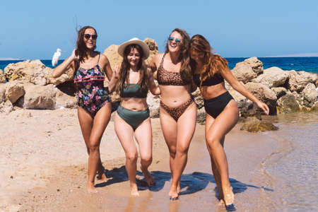 Group of beautiful young women strolling on a beach. Friends walking on the beach and laughing on a summer day.の写真素材