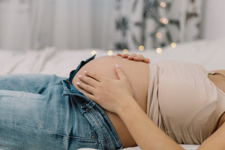 Attractive pregnant woman is sitting in bed and holding her belly. Pregnancy Concept.