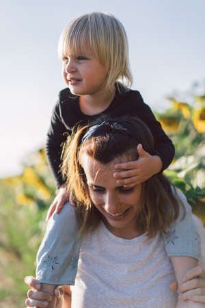 Young mother holding her baby. Mother and little daughter having good time in the Sunflower field. Mothers Day. Family conceptの写真素材
