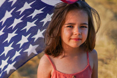 Happy little girl patriot running in the field with American flag. USA celebrate 4th of Julyの写真素材