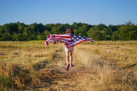 Happy little girl patriot running in the field with American flagの写真素材