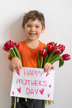 Cheerful happy child with tulips flower bouquet. Smiling little boy on white background. Mother's day conceptの写真素材