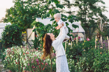Woman playing with her child in a greenhouse with flowers. Happy mother's day