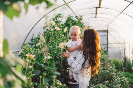 Woman playing with her child in a greenhouse with flowers. Happy mother's day