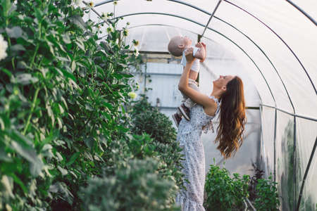 Woman playing with her child in a greenhouse with flowers. Happy mother's day