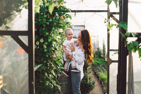 Woman playing with her child in a greenhouse with flowers. Happy mother's day