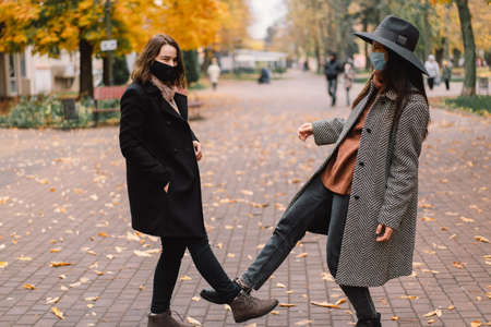 Physical distance and friendship safety greetings concept. Young women wearing face mask doing new social distancing greet with legs bumps for preventing virus spread.の写真素材