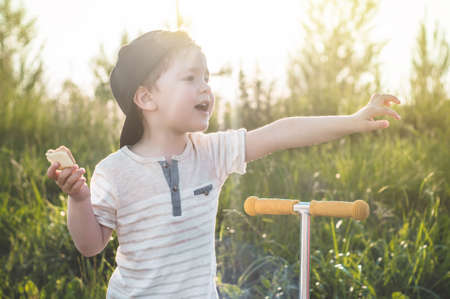 Happy Child eating and riding a scooter. Boy in the garden holding ice cream. Happy Boy kid eating ice cream.の写真素材