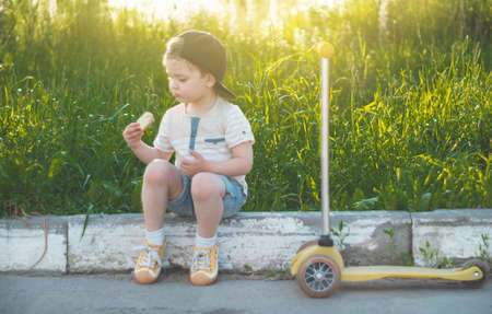 Happy Child eating and riding a scooter. Boy in the garden holding ice cream. Happy Boy kid eating ice cream.の写真素材