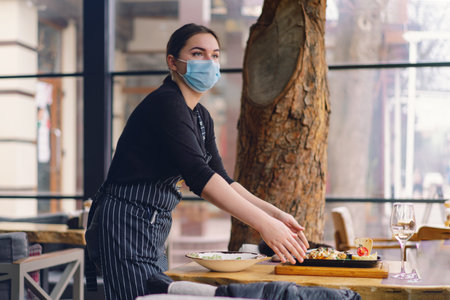 Waitress who wears a face mask is serving clients in a cafeの写真素材