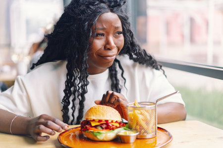 African woman with afro hair eating a tasty classic burger with fries.の写真素材