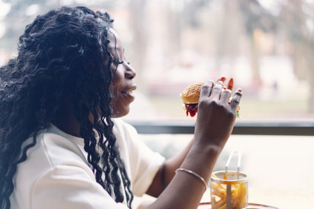 African woman with afro hair eating a tasty classic burger with fries.の写真素材
