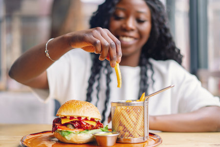 African woman with afro hair eating a tasty classic burger with fries.の写真素材