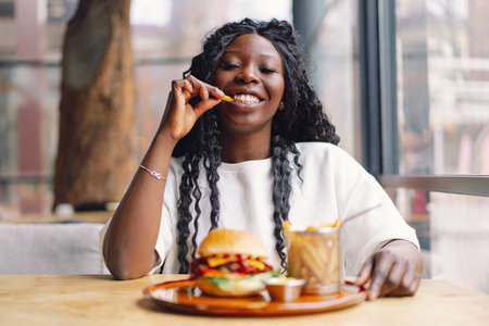 African woman with afro hair eating a tasty classic burger with fries.の写真素材