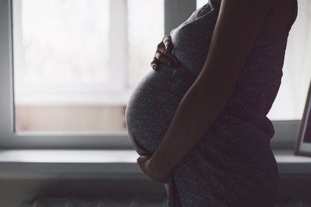 Happy Attractive pregnant woman standing near the window and holding her belly. Concepts of...