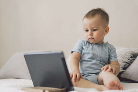 Little Boy sitting with a tablet in the room. The boy watching cartoons on the tablet. Technology...