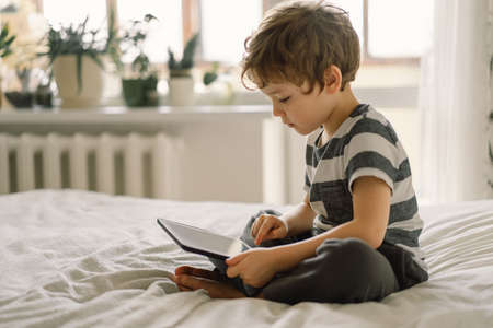 Little Boy with a tablet in the room. The boy play game on the tablet. Technology concept. Child with a gadgetの写真素材
